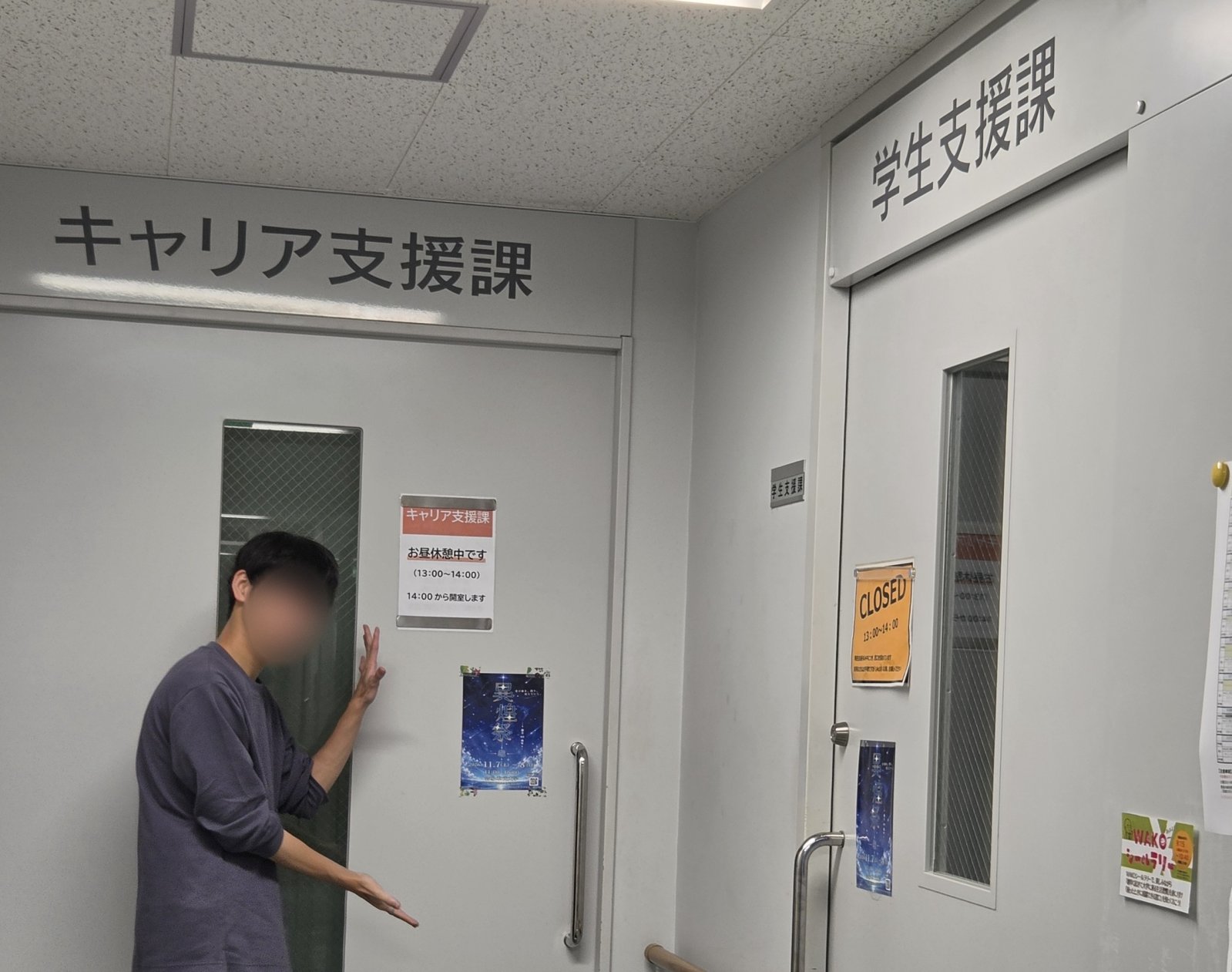「キャリア支援課」と「学生支援課」の入口のドアに貼った異煌祭 2026 のポスターと、ポスターを手で示す実行委員