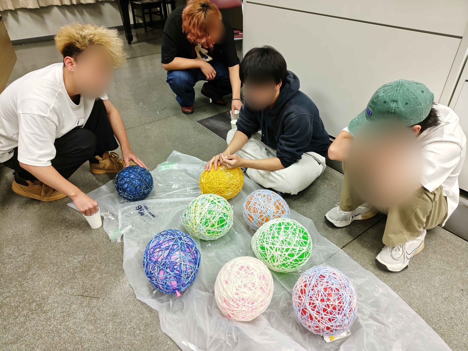 床に並んだ、色ちがいの毛糸を巻いた丸い飾りと、それを囲む実行委員