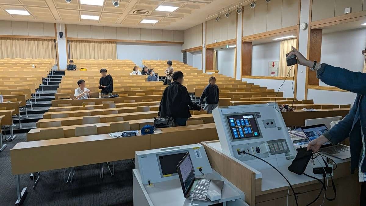 J401の教卓で、映像の機器とつなぐ線を確かめるスタッフ